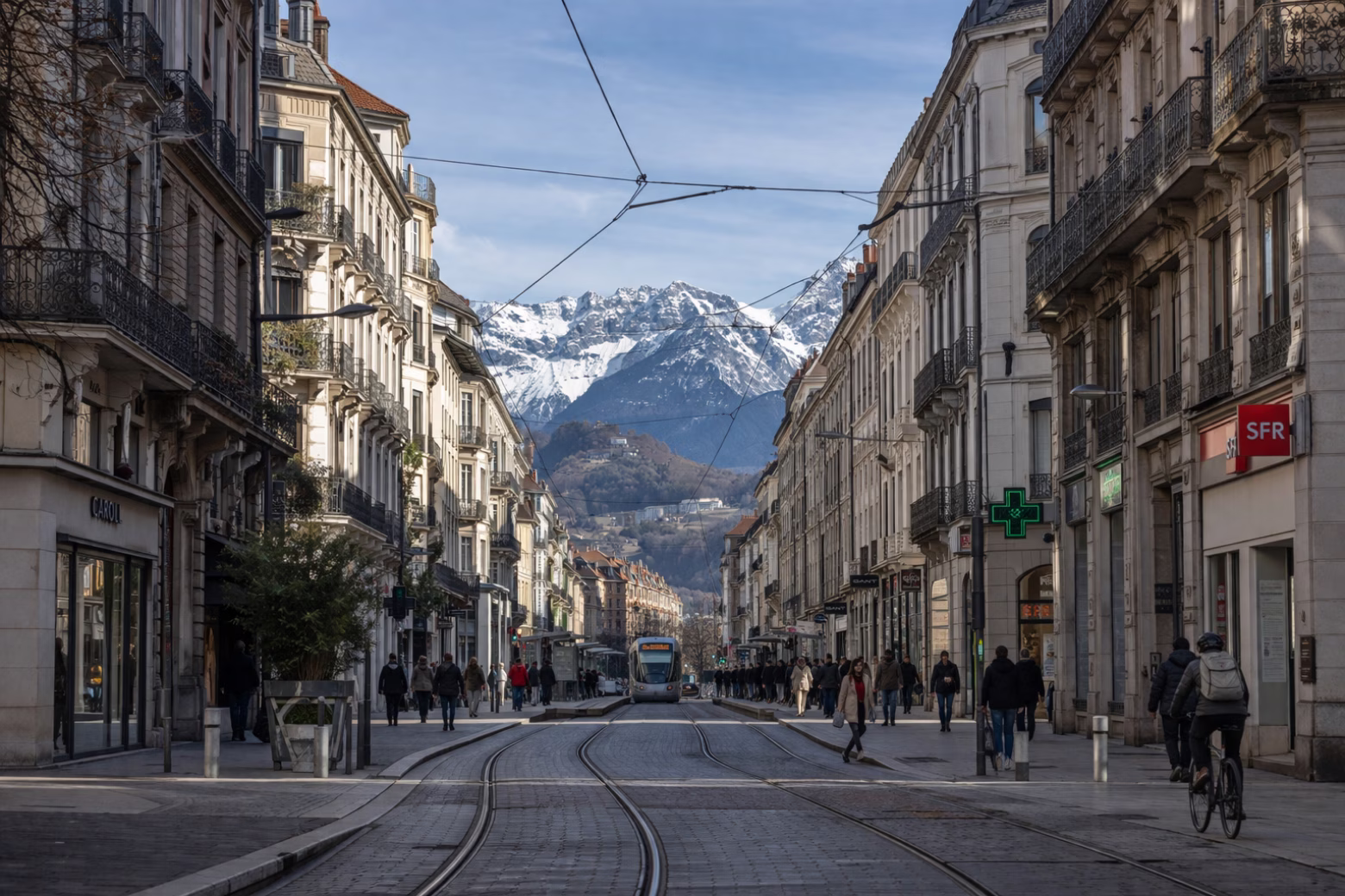 A tram-lined city street with mountains in the background